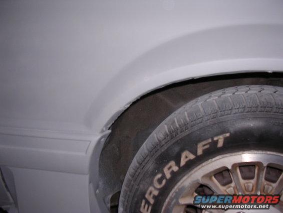 Close-up of a car's wheel well and tire with "SUPERMOTORS" visible on the tire