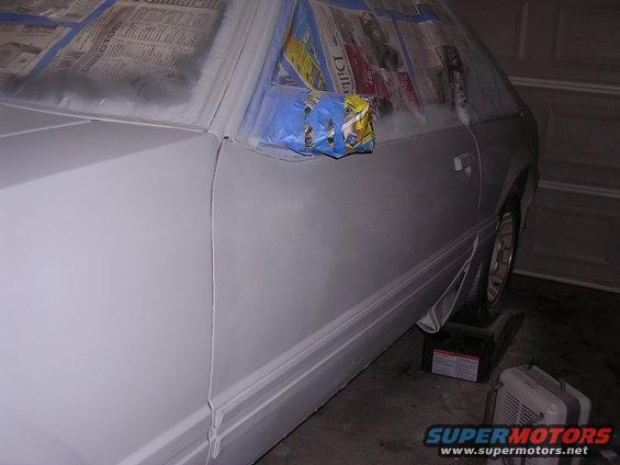 White car body, masked with newspaper and tape, on jack stands in a garage
