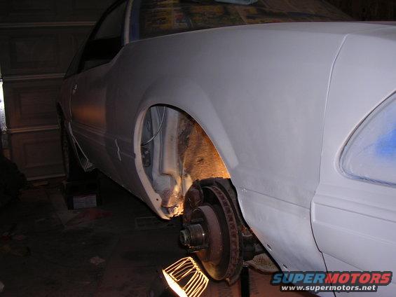 Car body primed, front wheel well exposed, brake rotor visible
