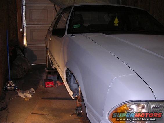White coupe in garage, front fender removed, jack stands under car