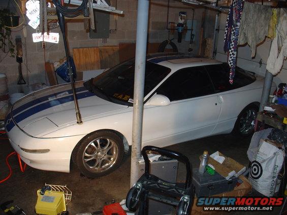 White 1993 Ford Probe coupe with blue racing stripes parked in a garage