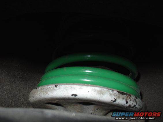 Green coil spring on a white suspension component, close-up view