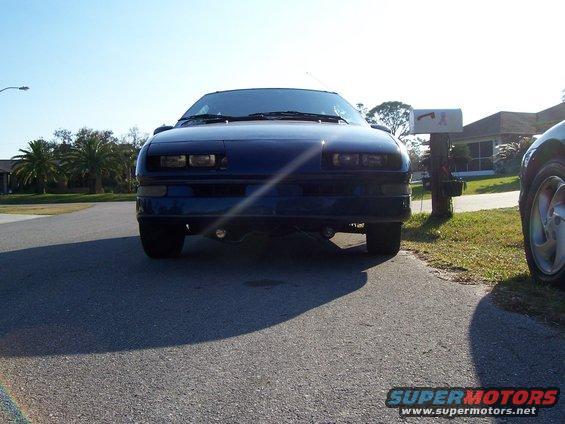 Front view of a dark blue coupe parked on a driveway. Another car is partially visible on the right. A mailbox stands nearby