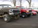 1978 Ford Bronco - Two lifted Ford trucks are parked side-by-side, with other vehicles in the background.