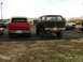 1978 Ford Bronco - Two SUVs are parked in a lot with other vehicles and school buses in the background.