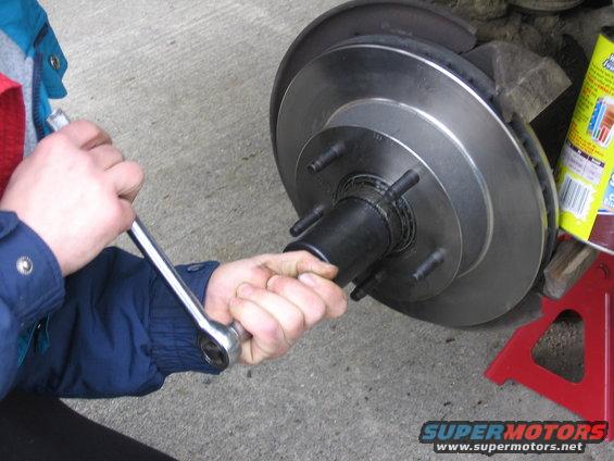 Close-up of a car's brake rotor and hub assembly being worked on with a wrench