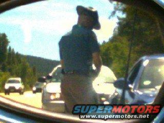 Reflection of man in cowboy hat in side mirror, other cars visible on road
