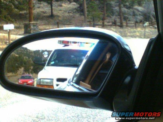 Side mirror view shows an ambulance with emergency lights and a red car behind it