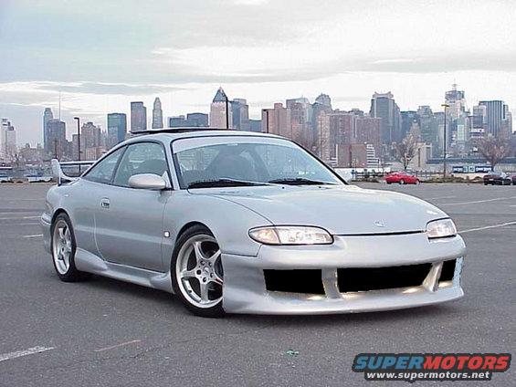 Silver coupe with aftermarket body kit and spoiler, city skyline in background