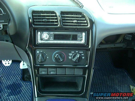 Car interior showing JVC stereo, climate controls, and dashboard vents. Blue floor mats visible