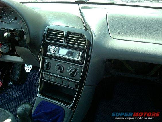 Car interior dashboard with aftermarket stereo, vents, and climate controls. The driver's side instrument cluster is partially disassembled