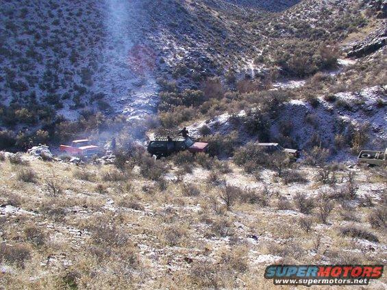 Several off-road vehicles are parked on a snowy, brush-covered hillside