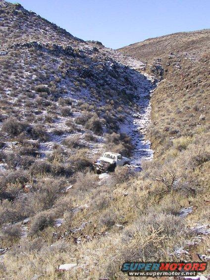 White pickup truck stuck in a dry creek bed with snow on the hillsides