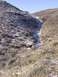 1978 Ford Bronco - A white pickup truck is stuck in a dry creek bed, surrounded by sparse vegetation and patches of snow on the surrounding hills.