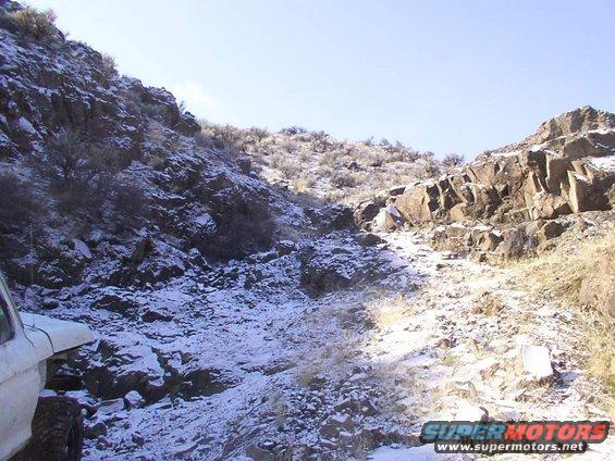 Snowy mountain trail with a white vehicle fender and tire visible on the left