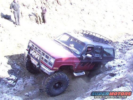 Red and black off-road SUV climbing a rocky incline with a roof rack