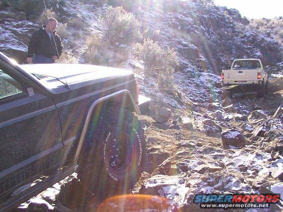 Dark green Jeep Cherokee XJ and a white pickup truck on a rocky, snowy trail