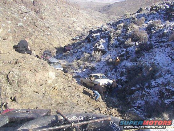 Off-road vehicles in a snowy ravine, one truck being winched