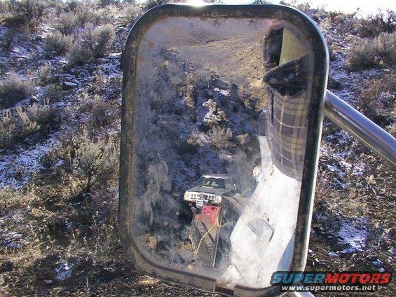 reflection in side mirror shows blurry landscape and sky