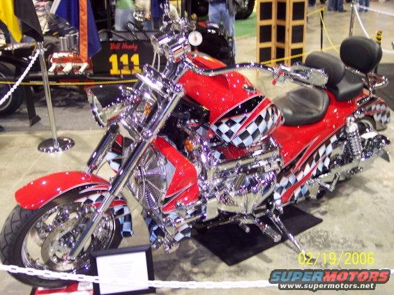 Red motorcycle with checkerboard graphics and chrome accents, viewed from the front three-quarter angle