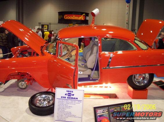 Orange 1955 Chevrolet 210 Sedan with doors and hood open, sitting on display