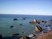 1989 Ford Bronco - A scenic view of a rocky coastline with waves crashing against the shore under a bright blue sky.