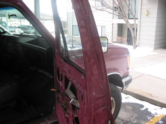 Interior of a maroon truck with the driver's door open, showing the dashboard and door panel removed