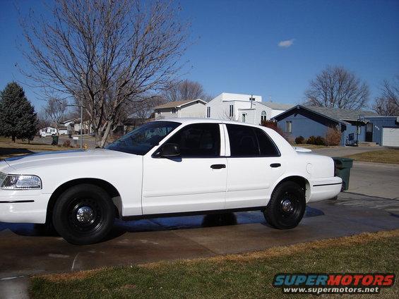 Side view of a white 2000 Ford Crown Victoria with black steel wheels parked in a driveway