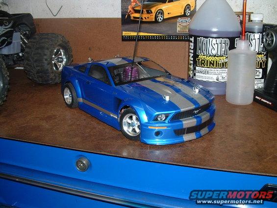 Blue remote control car with silver stripes, parked next to a monster truck