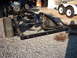 1964 Ford Galaxie - The chassis of a vehicle, including the engine and tires, is shown from a side angle on a gravel surface.