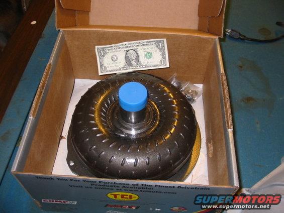 Torque converter with blue cap in a box, next to a dollar bill