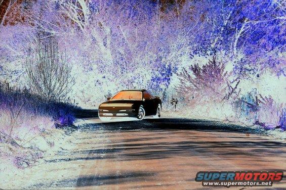 Front view of a black 1993 Mazda MX-6 driving on a dirt road surrounded by trees