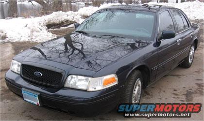 Dark blue Ford Crown Victoria, front 3/4 view, parked on asphalt with snow in background
