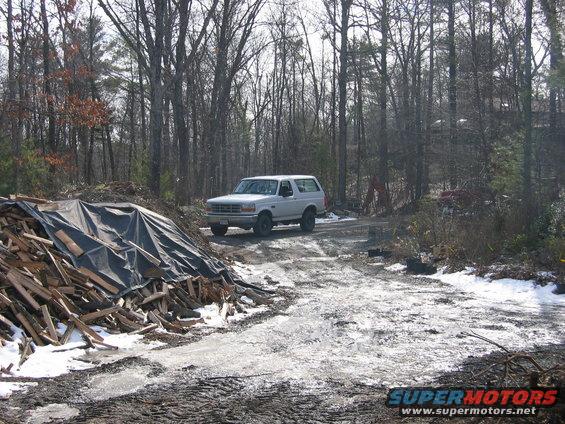 1995 Ford Bronco parked on a dirt road in a wooded area with a pile of lumber to the left