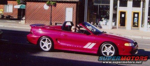 Pink convertible sports car driving down a street, driver visible