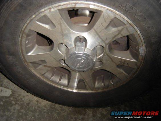 Close-up of a silver alloy wheel with a black tire. Center cap has text