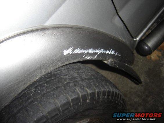 Close-up of a silver vehicle's rear fender with white scratches over the tire
