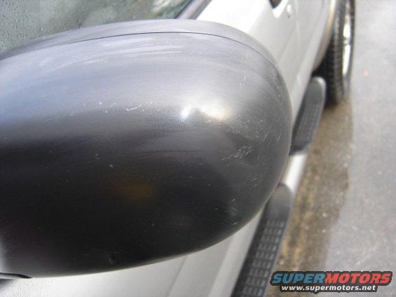 Close-up of a black side mirror with minor scuffs on a silver vehicle. Running boards are visible below