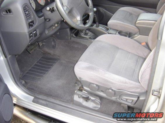 Interior of a silver SUV, showing driver's seat, dashboard, and center console. The vehicle has grey cloth seats and a black floor mat