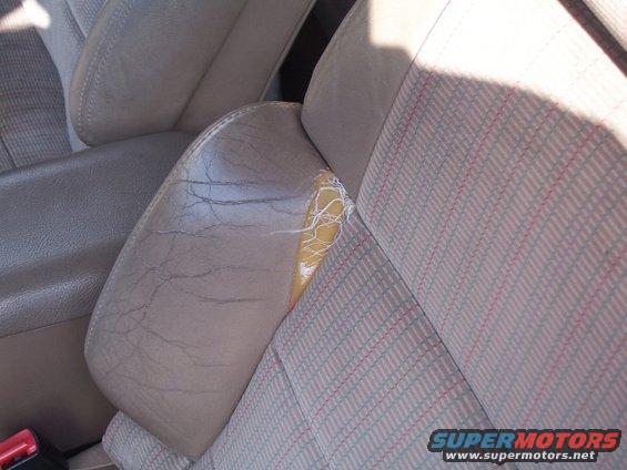 Driver's seat with cracked leather and a large tear showing yellow padding. Fabric seatback has a red and blue striped pattern