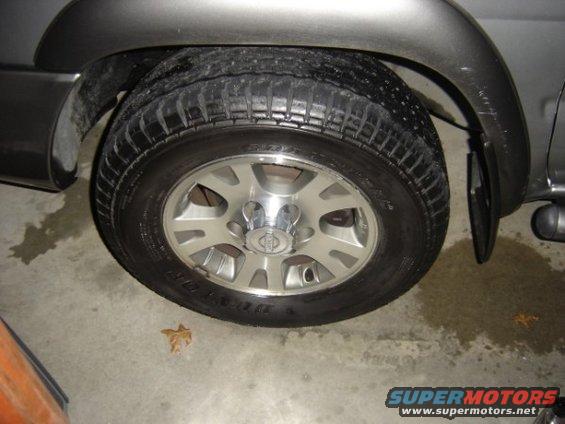 Close-up of a Nissan wheel and tire on a vehicle. The wheel has five spokes and a center cap with the Nissan logo