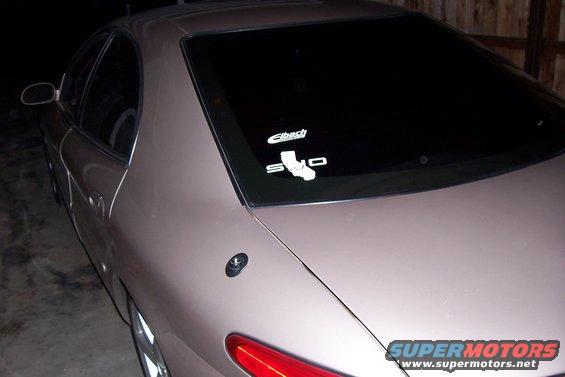 Car's rear quarter panel and tinted rear window with Eibach and S.I.D. stickers. A red taillight is visible