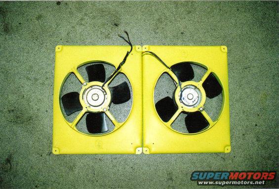 Two yellow electric fans side-by-side on a green surface