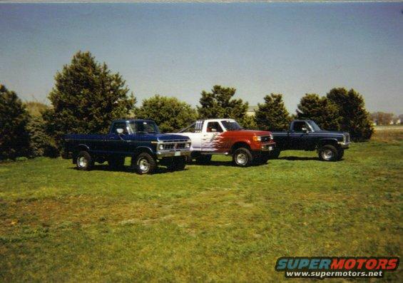 Three pickup trucks parked in a grassy field under a clear blue sky