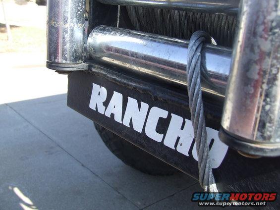 Close-up of a winch with "RANCH" written on the bumper. Cable is wrapped around a roller