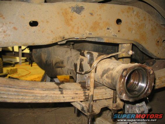 Close-up of a vehicle's rear axle assembly and leaf springs, showing rust on the frame