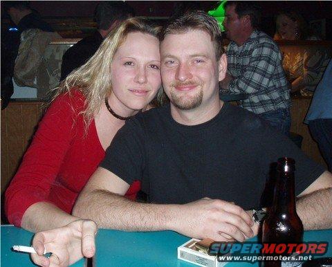 Couple posing for a photo in a bar with a cigarette and beer bottle on the table