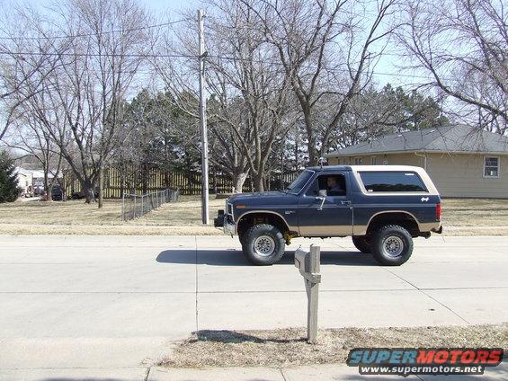Dark blue and tan Ford Bronco driving on a street, side view