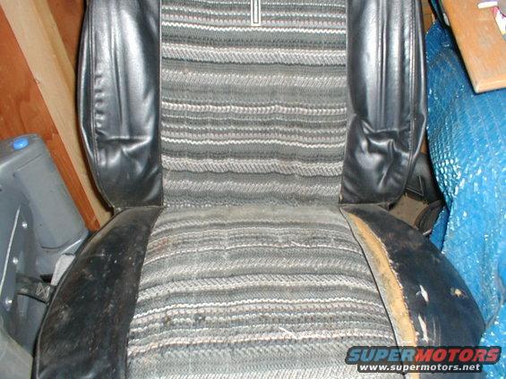 Close-up of a worn car seat with striped fabric and black vinyl bolsters. The seat shows signs of damage and age