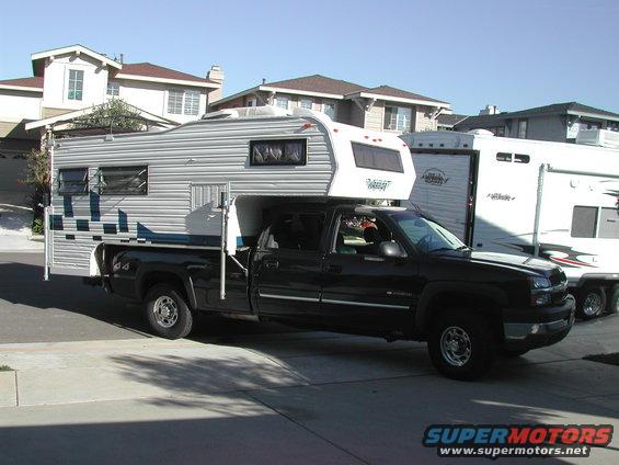 Black pickup truck with camper shell and trailer, 3/4 front view